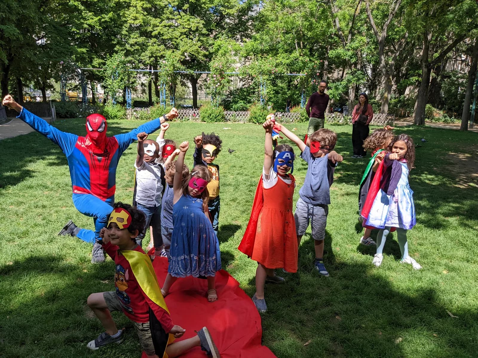 Un animateur en costume de Spider-Man saute au milieu d’enfants masqués, bras levés, dans un parc