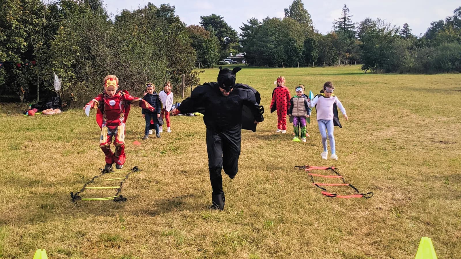 Des enfants costumés en super-héros s’élancent sur un parcours d’agilité au milieu d’une prairie