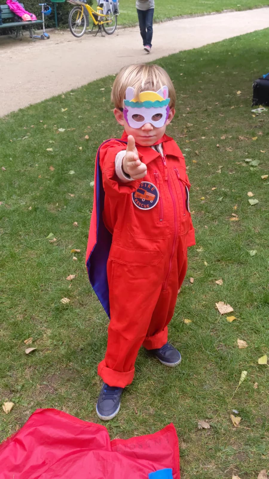 A child in a superhero cape and mask giving a thumbs up