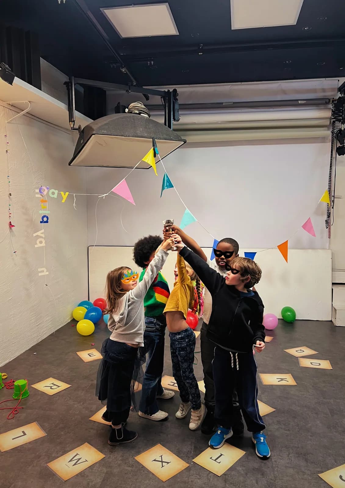 Children joining hands in the middle of a room decorated with bunting and balloons