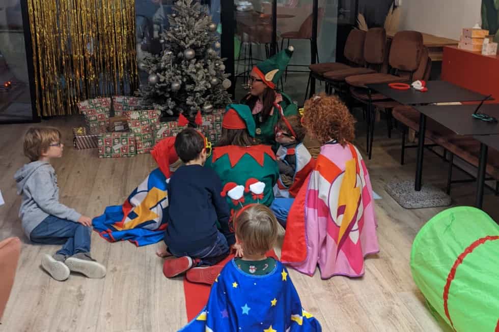 A Kidays host dressed as an elf telling a story to children in front of a tree and presents