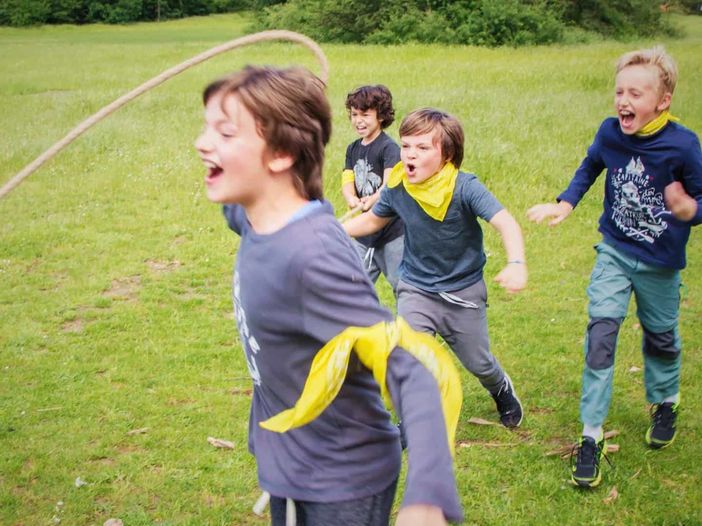 Children in yellow neckerchiefs running and laughing across a lawn during an outdoor game.