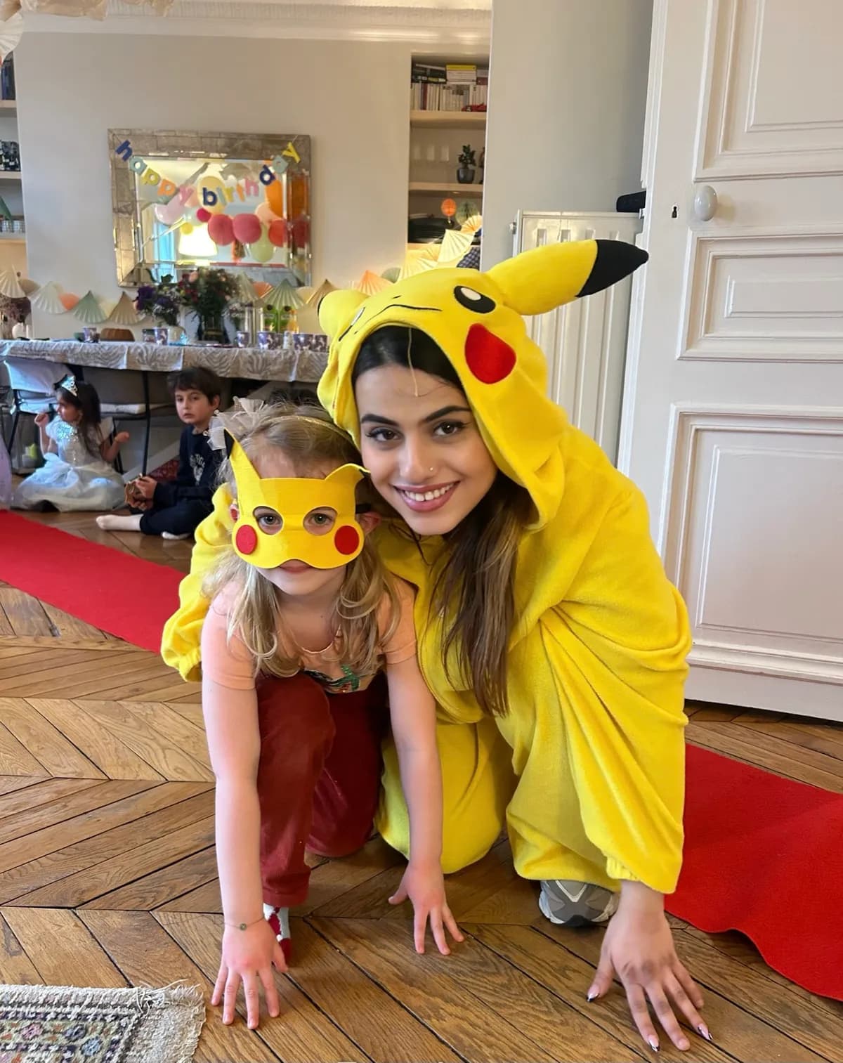 Une animatrice en costume de Pikachu pose avec une petite fille masquée sur le parquet d’un appartement parisien.